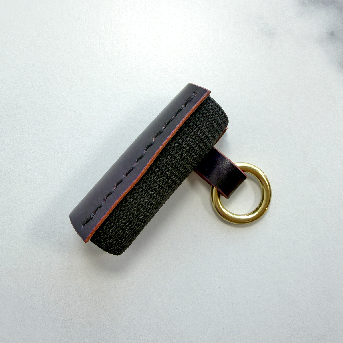 A purple leather lip balm holder with an elastic back and a brass ring to attach to a key chain on a white background.