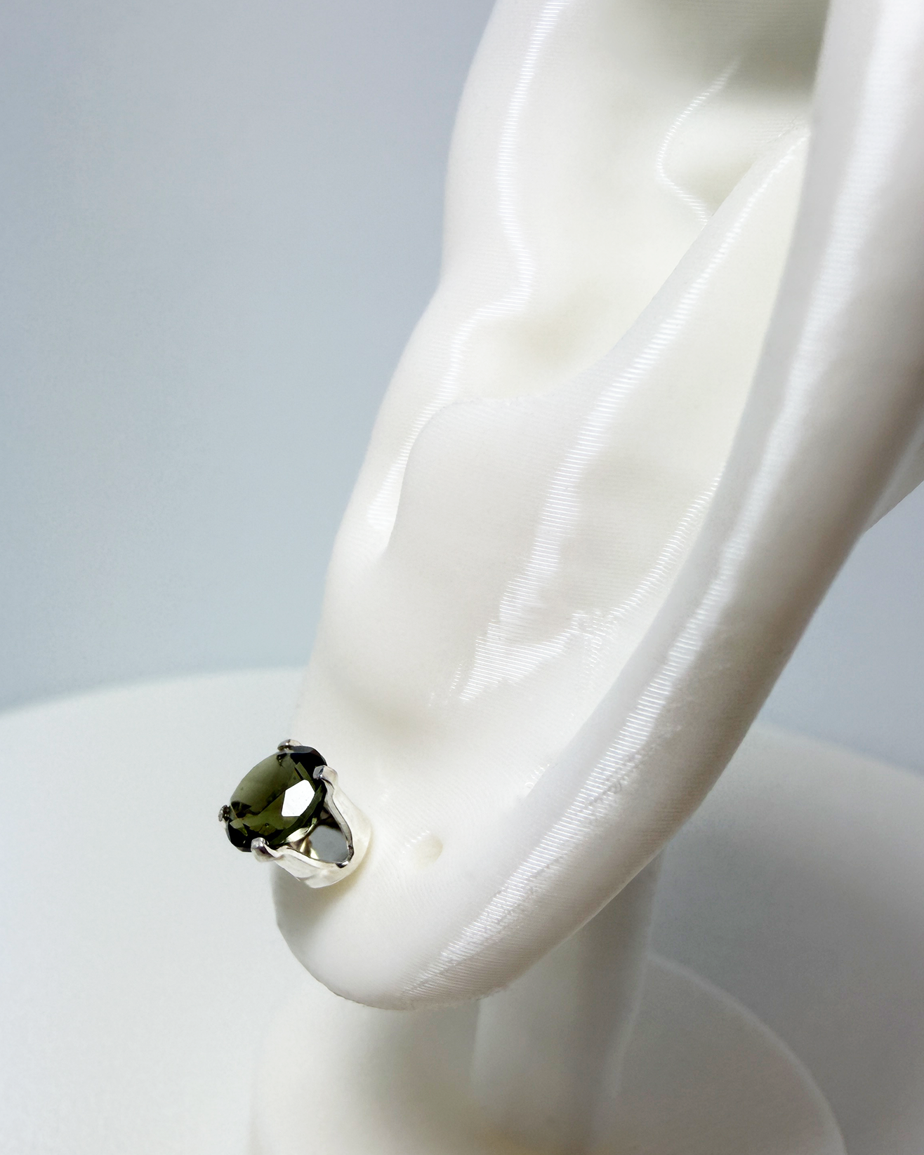 A side view of a green Moldavite gemstone post earring on a white mannequin ear