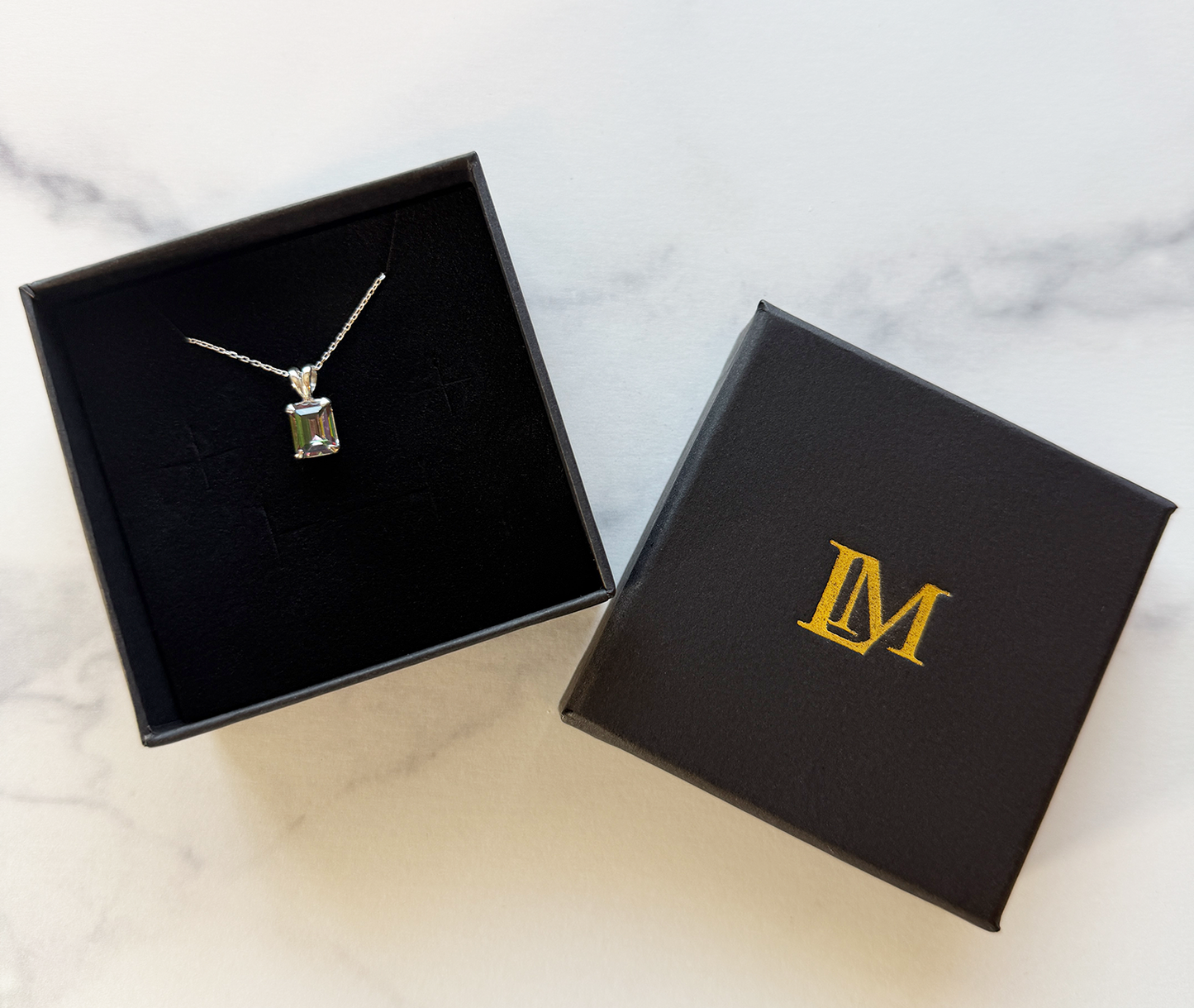 Jewelry box with a sterling silver necklace with a mystic quartz pendant and a LM branded box on a marble surface