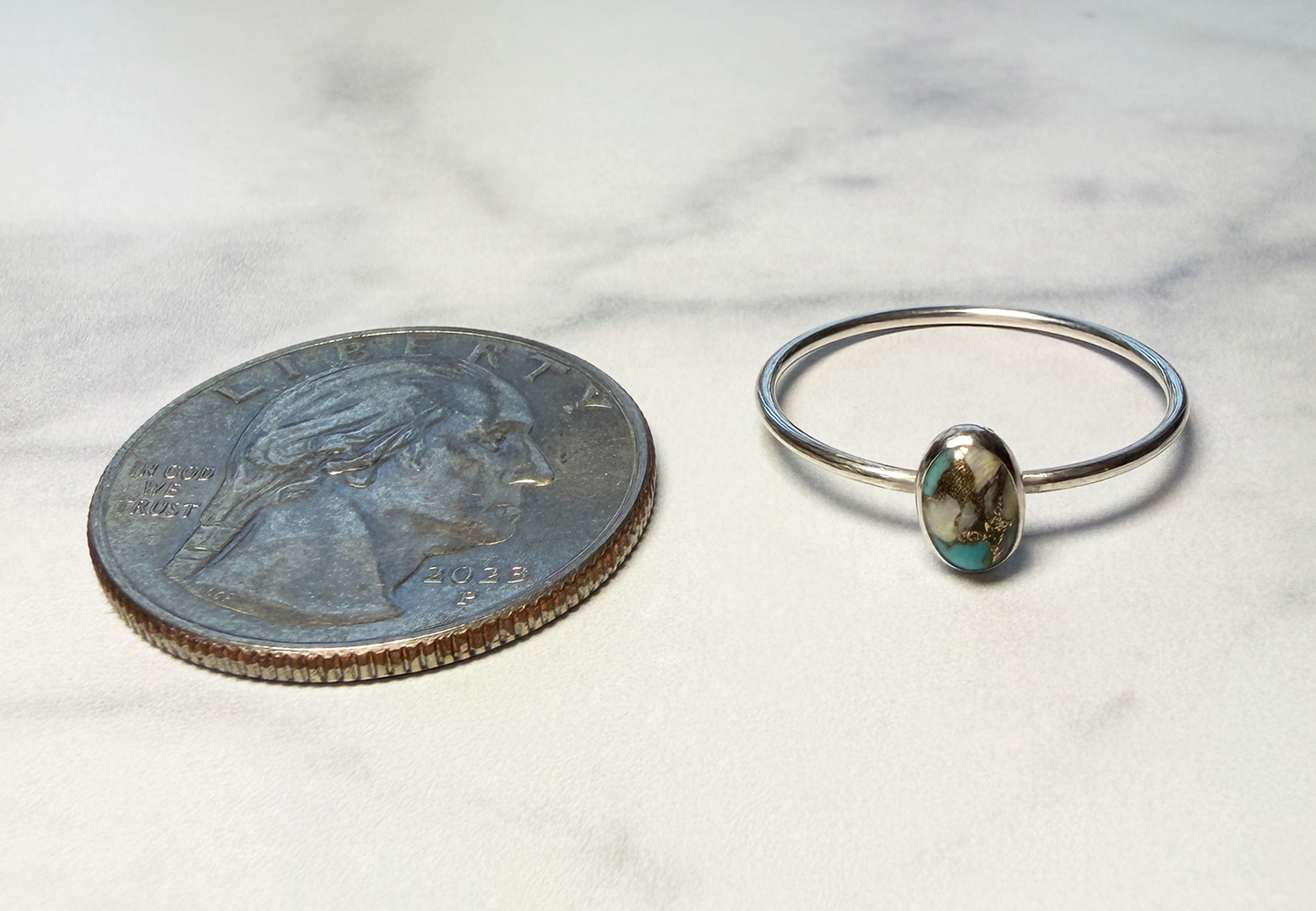 Sterling silver ring with turquoise stone next to a quarter for scale on a white background