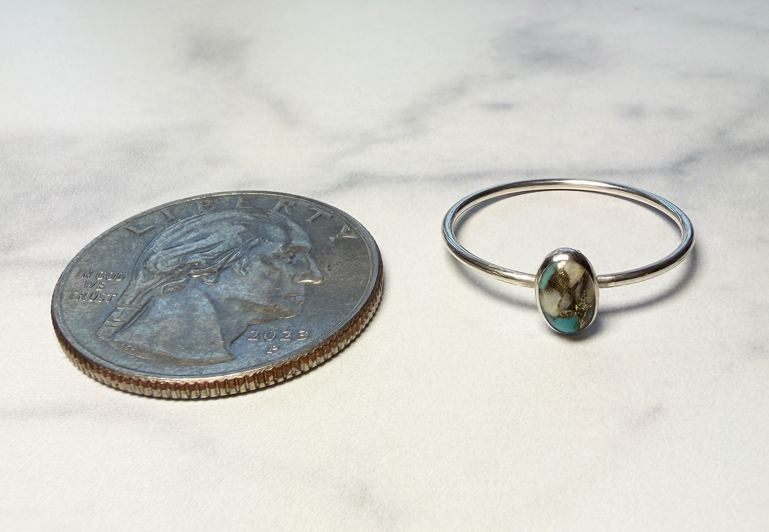Sterling silver ring with turquoise stone next to a quarter for scale on a white background
