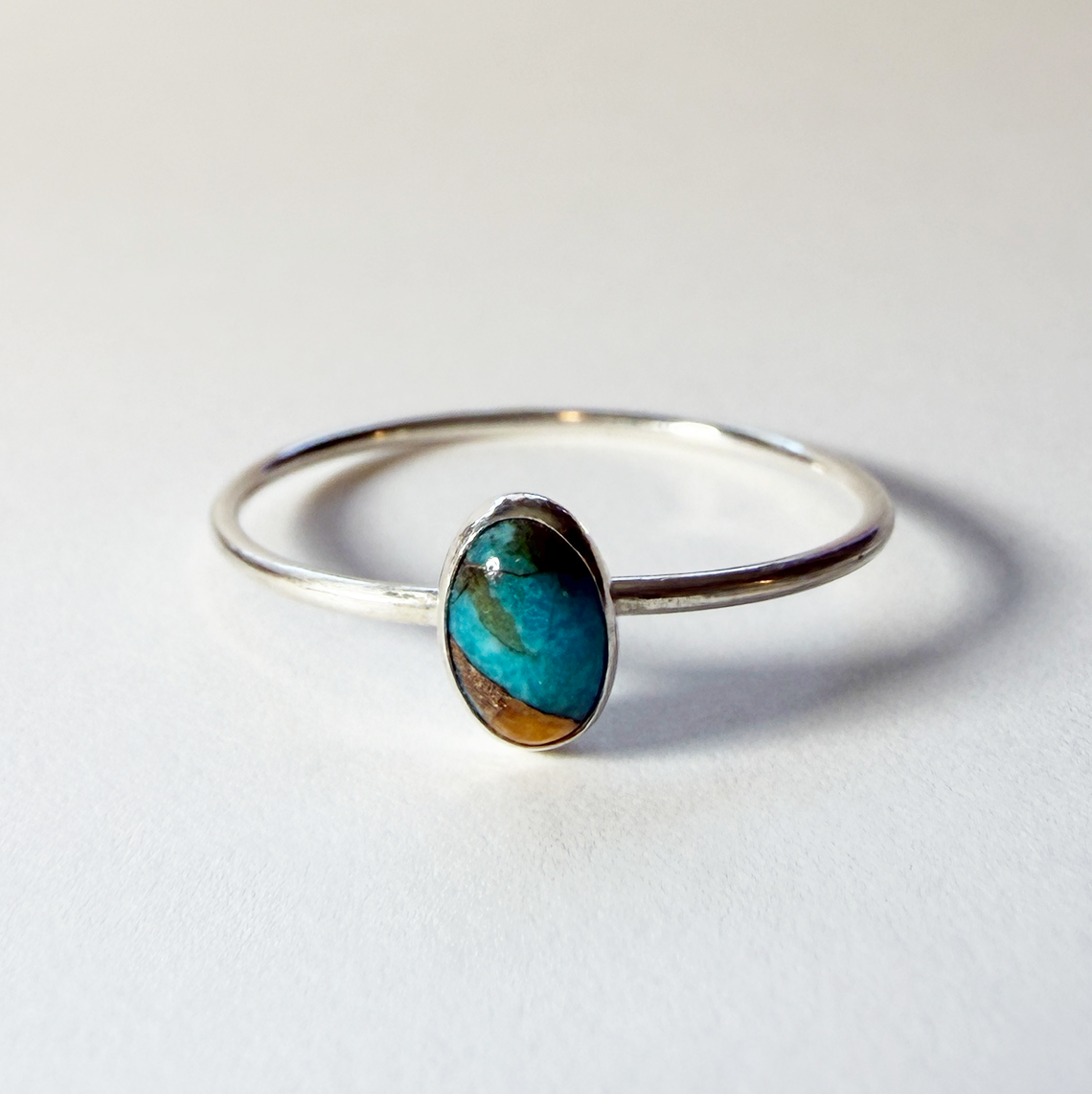 Sterling silver ring with an orange and teal turquoise stone on a white background
