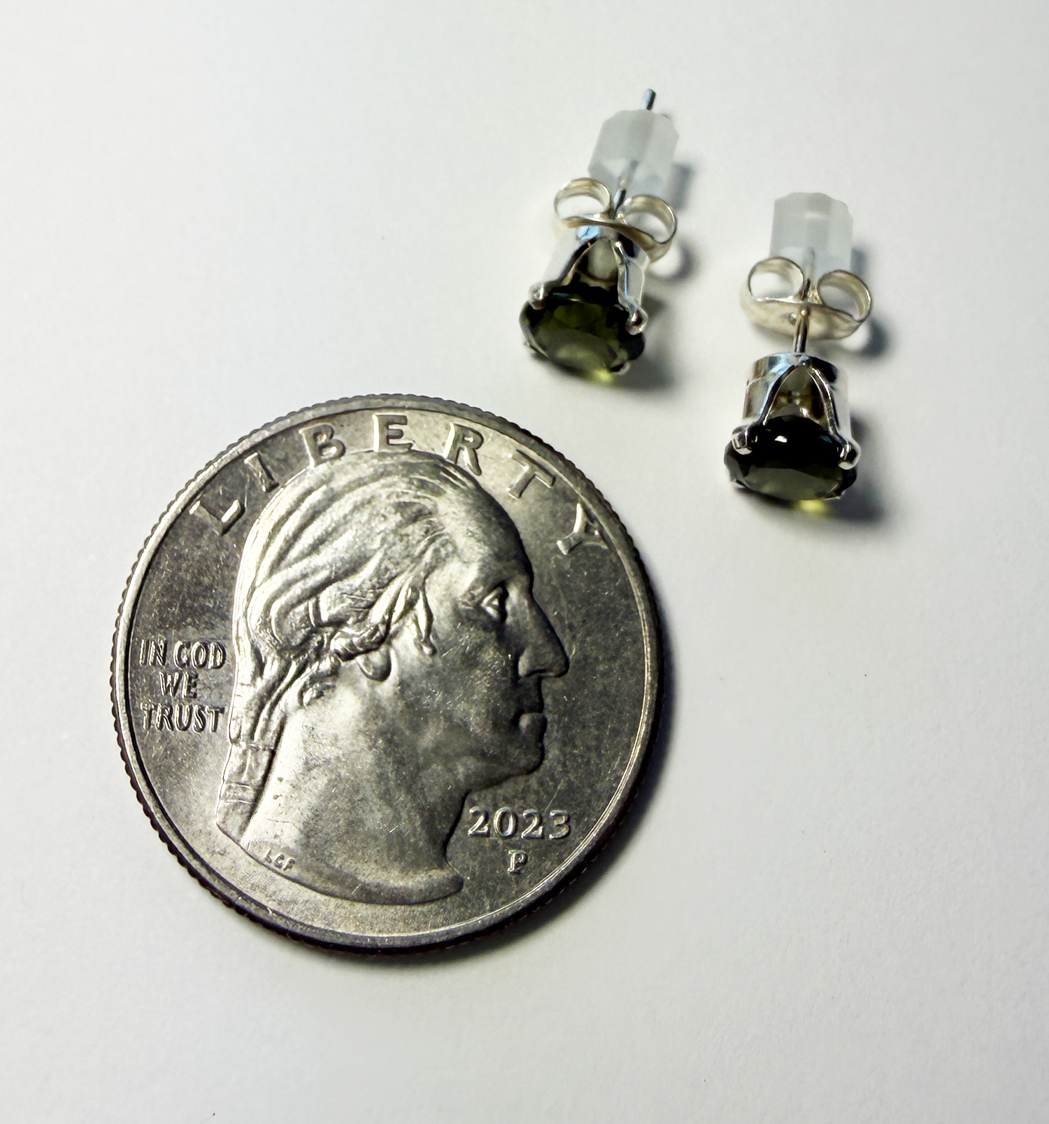 Pair of stud earrings with green Moldavite gemstones next to a quarter for scale