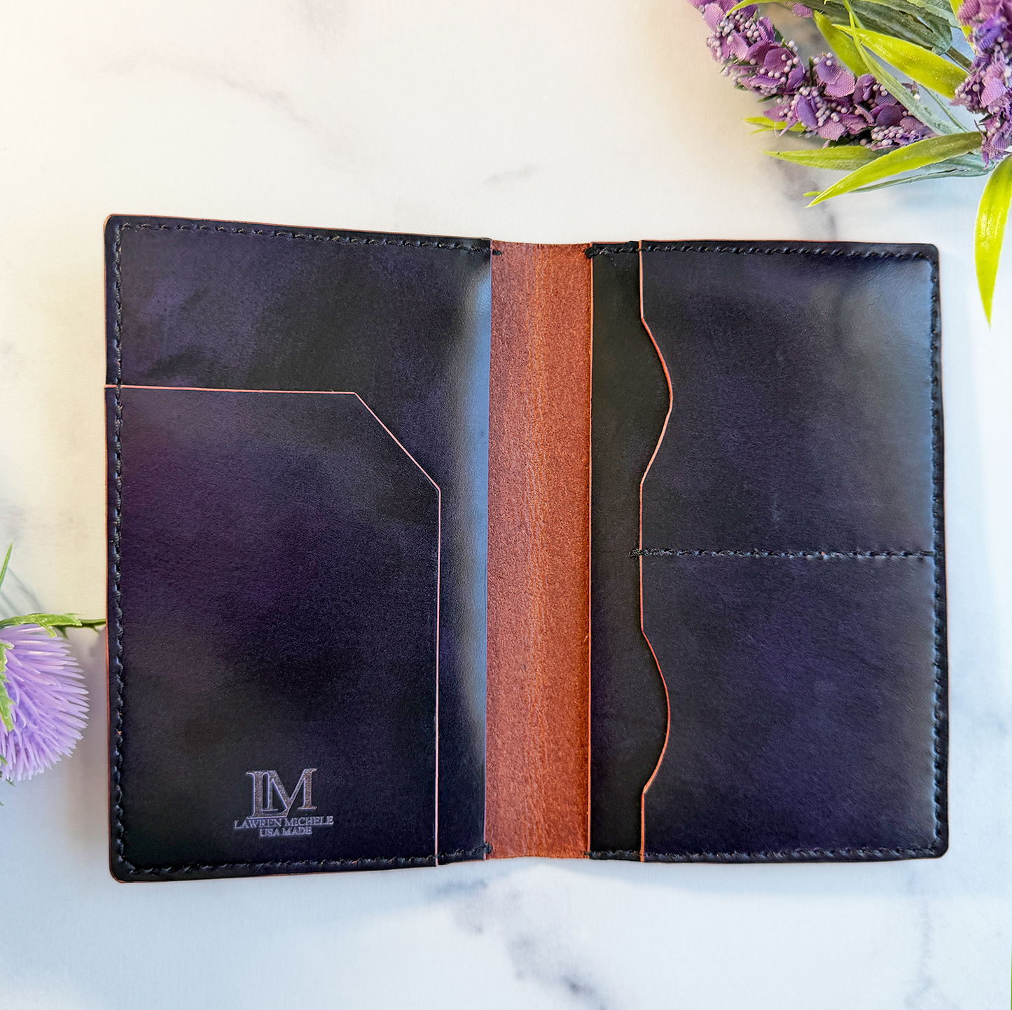 A purple leather passport cover on a marble countertop. It's open to show pockets to hold a passport, cards, cash, and a plane ticket. There is a small logo engraved on the inside. 