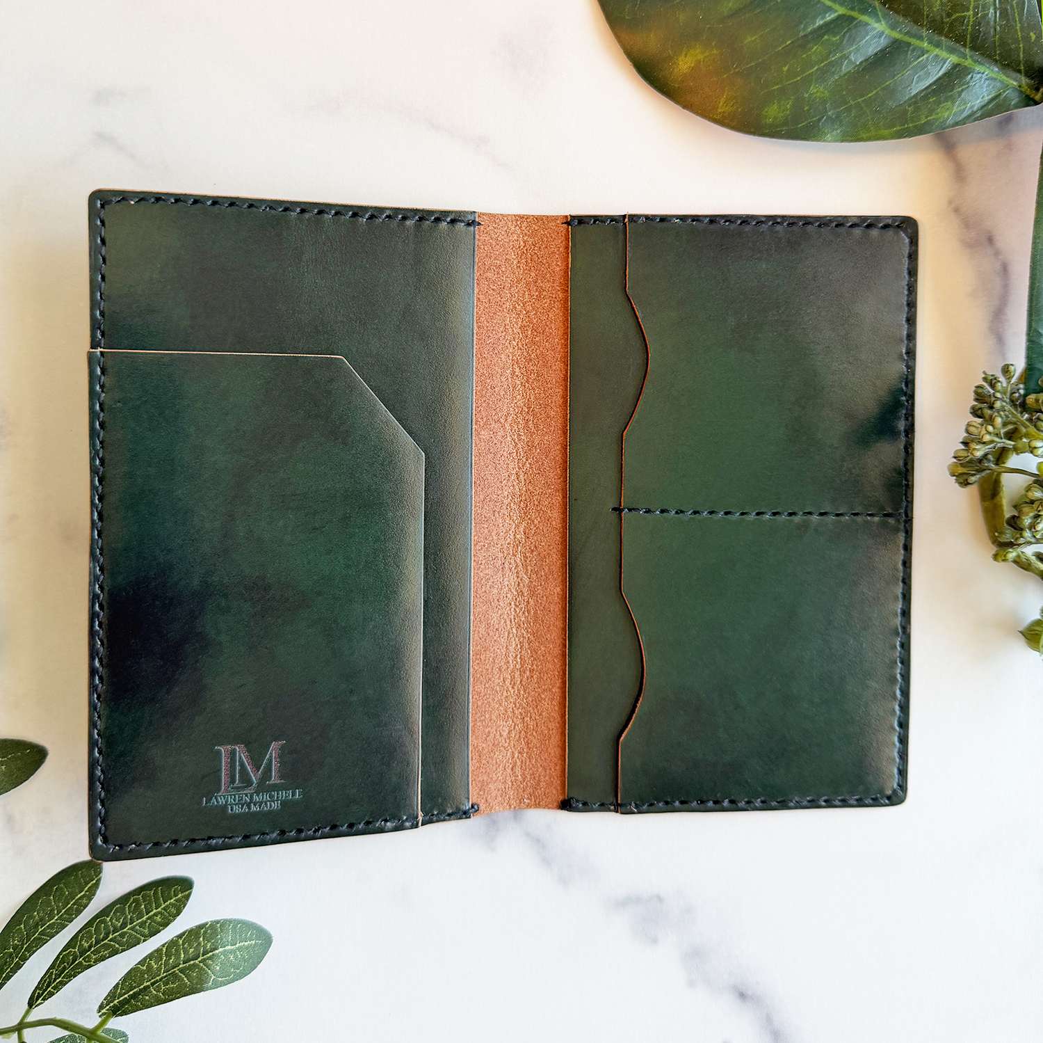 A green leather passport cover on a white marble countertop. It's open to show pockets for a passport, plane ticket, cash, and up to four credit cards.