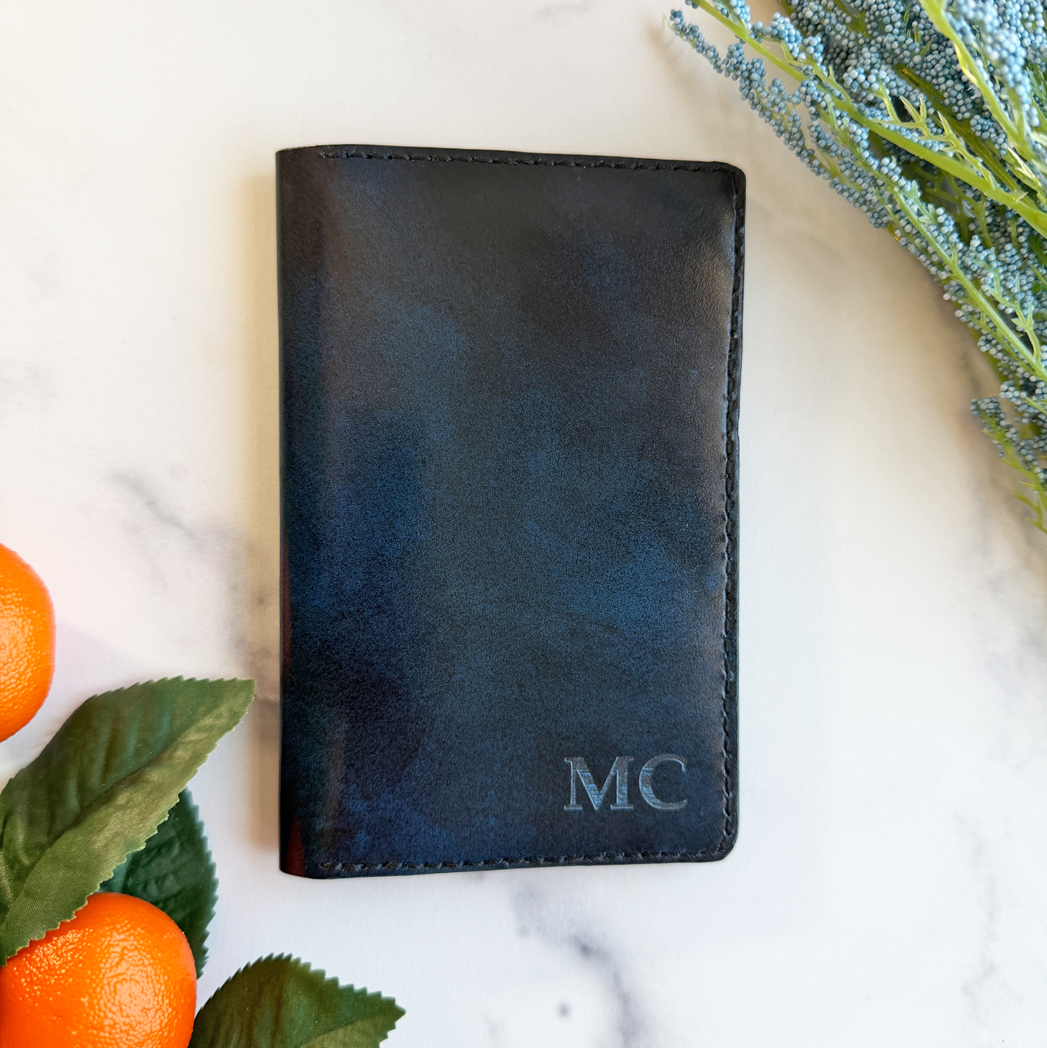 A blue leather passport cover on a marble countertop with initials engraved on the bottom right corner. 
