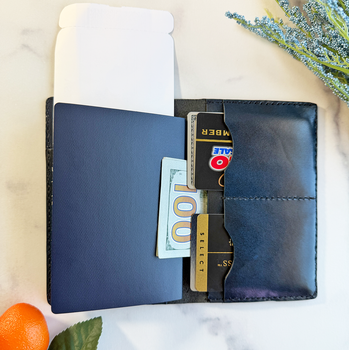 A blue leather passport cover on a marble countertop. The passport is open and contains a passport, four cards, cash and a plane ticket.