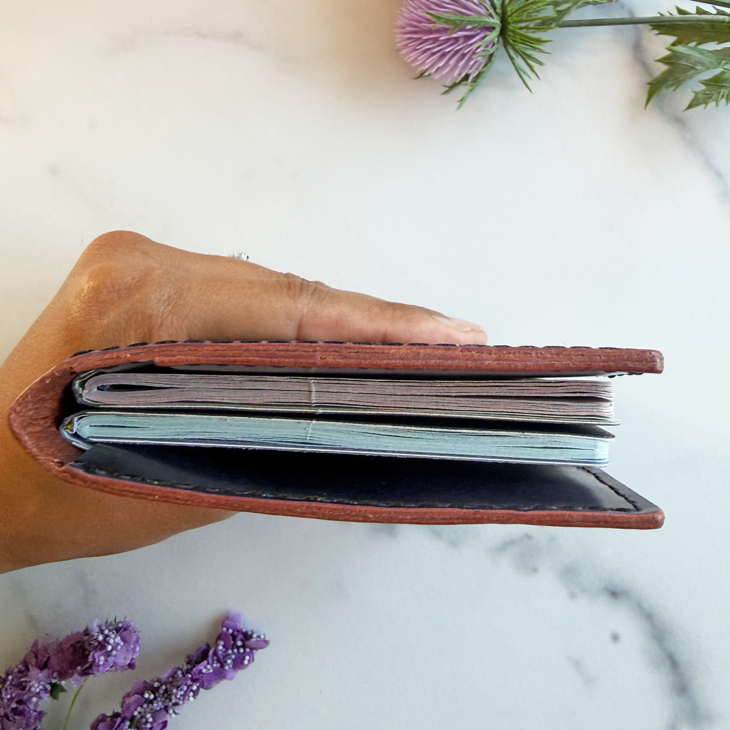 A top view of a leather passport holder showing two passports inside. A hand is holding the passport cover to show thickness. 